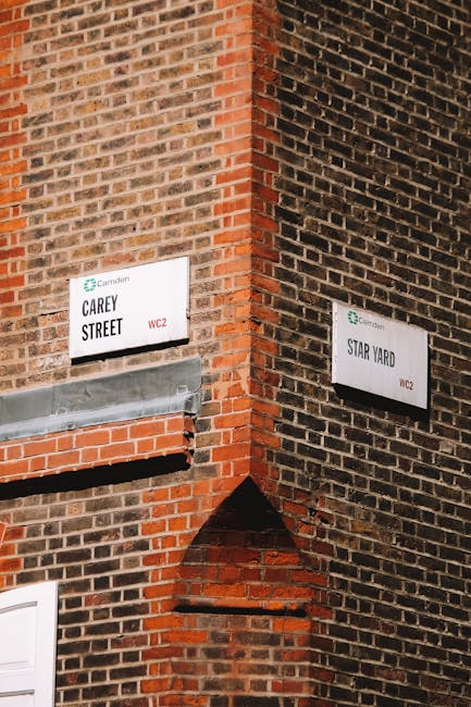 Photograph of the corner of a red brick building displaying two street signs for Carey Street and Star Yard, located in Camden with the signs indicating their location within WC2. The Carey Street sign is mounted on the left side, with a grey metal guttering beneath it, while the Star Yard sign is on the right side of the building. The brickwork shows weathered, reddish-brown bricks with some varying shades, and the signs are white with black text and a small green Camden Council logo in the corner. The image captures the building's exterior in daylight, highlighting the urban atmosphere typical for house removals or moving logistics context while the site appears ready for packing or furniture transport tasks.
